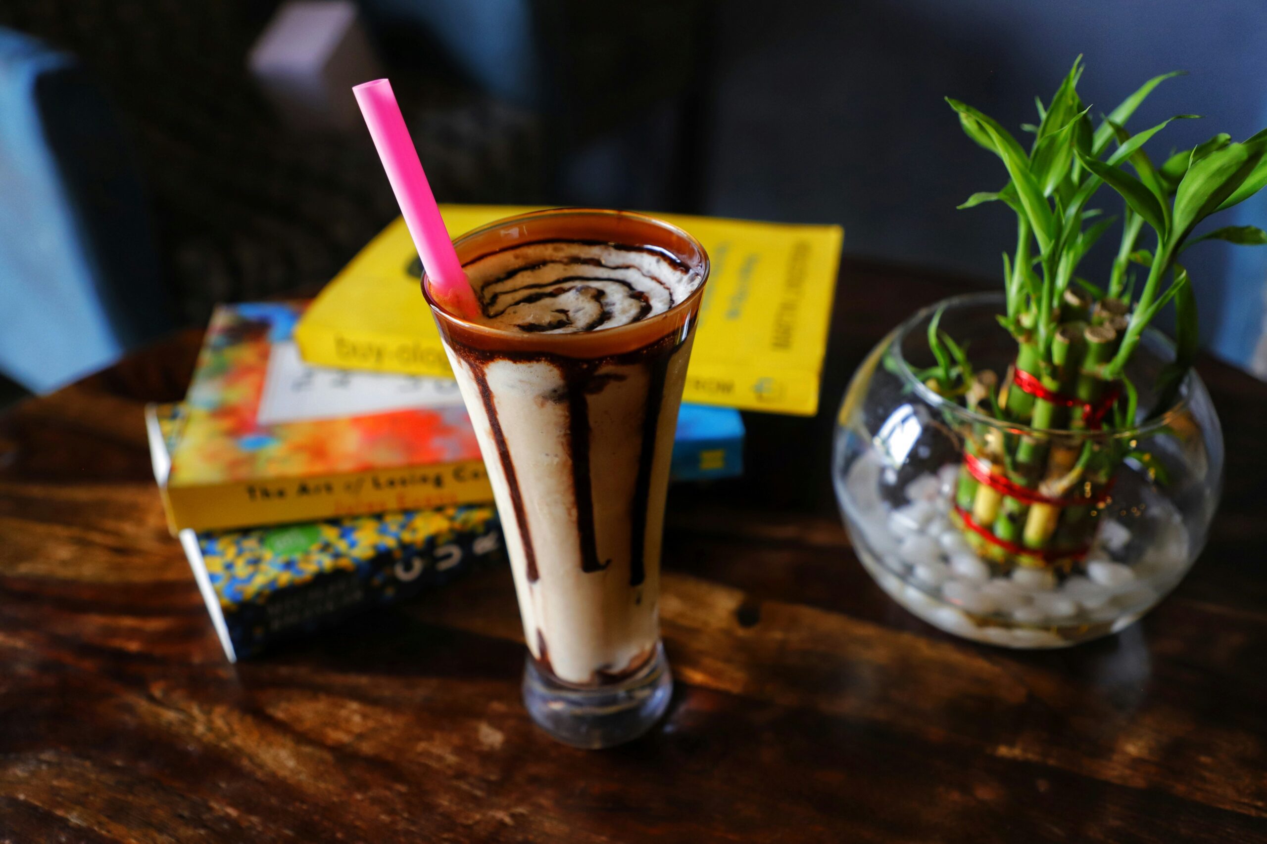 Books, milkshake with a pink straw, bamboo in a glass jar with stones.